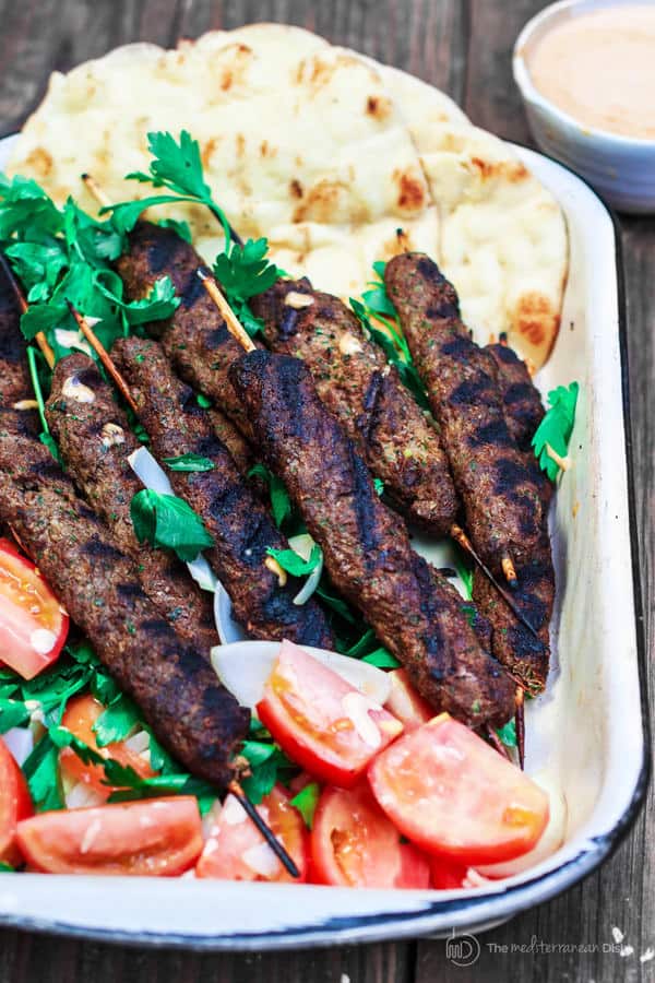 a dish with kebabs, pita bread, and quartered tomatoes