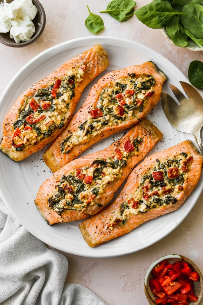 four pieces of stuffed salmon with spinach, tomatoes, and feta on a white plate