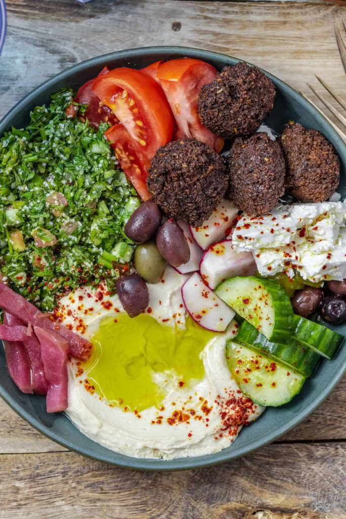 a falafel bowl with hummus, cucumber, tomatoes, onions, falafel, and more