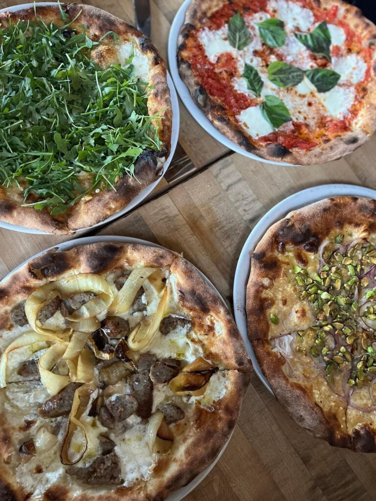Four dinner party personal pizzas on a wooden table. Each one having an array of different toppings.