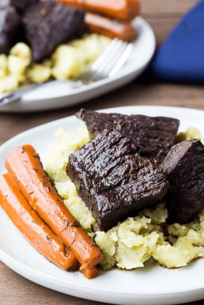 Braised Short ribs, carrots, and mashed potaotes on a plate