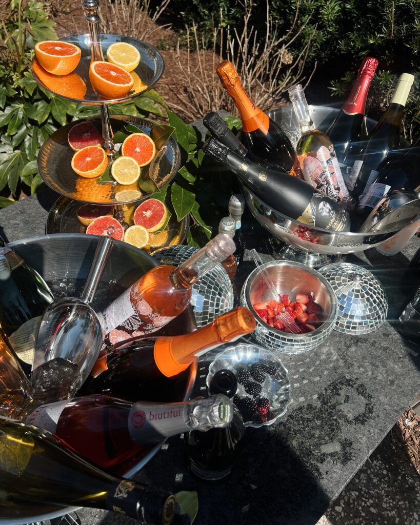 Outdoor hosting essentials photo of buckets of champagne and wine on ice and oranges with greenery for decor