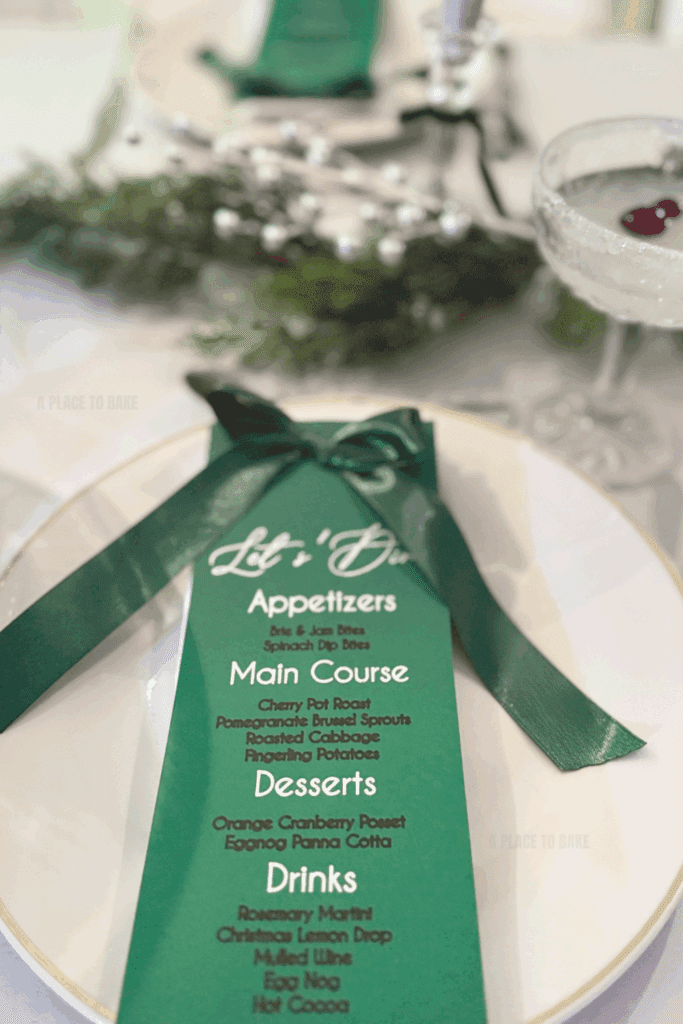 An image of a table setting with a green menu and silver holiday table decor, and a cocktail with cranberries in it